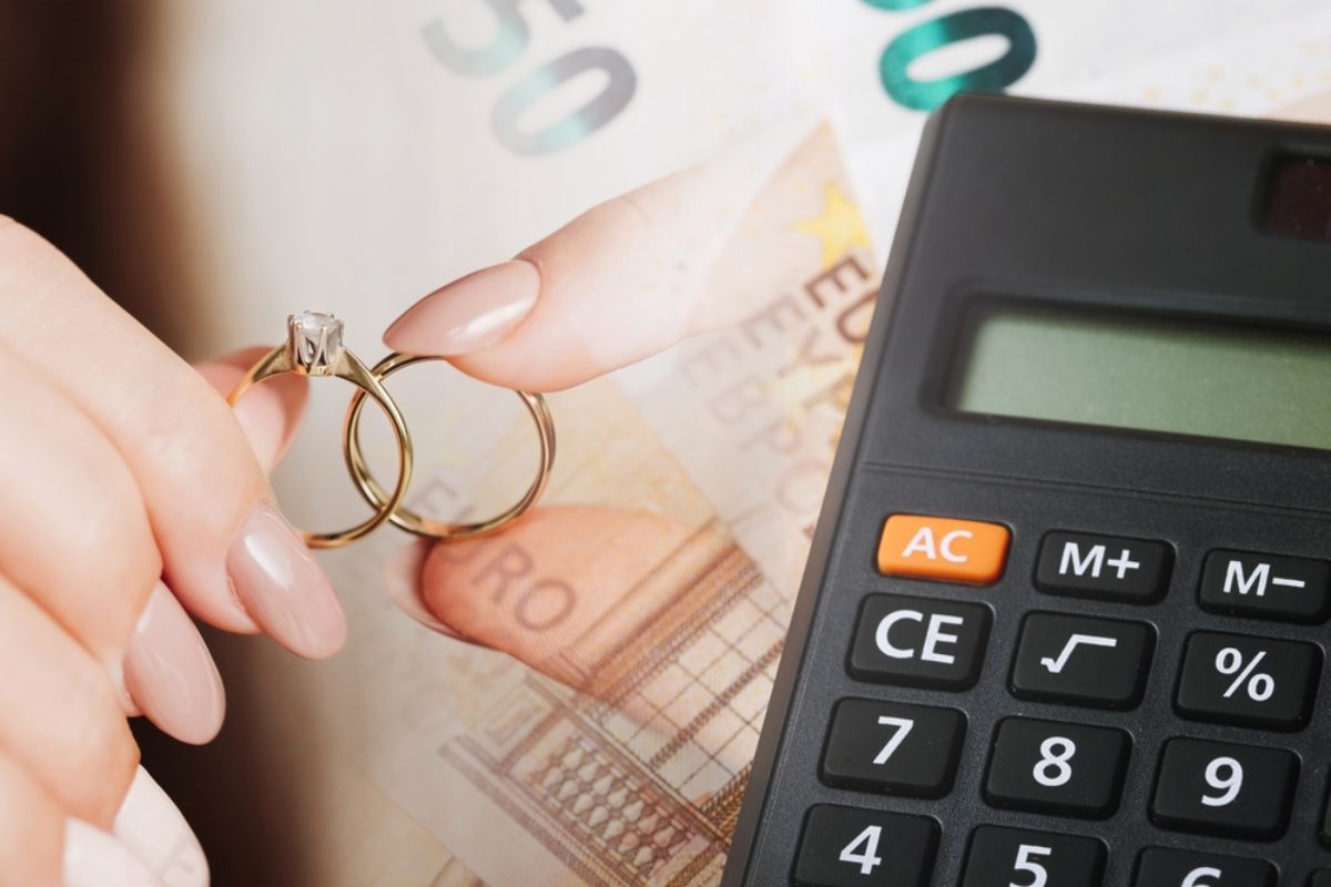 A calculator and two hands hold wedding bands, symbolizing couples questioning how much should you spend on a wedding ring.