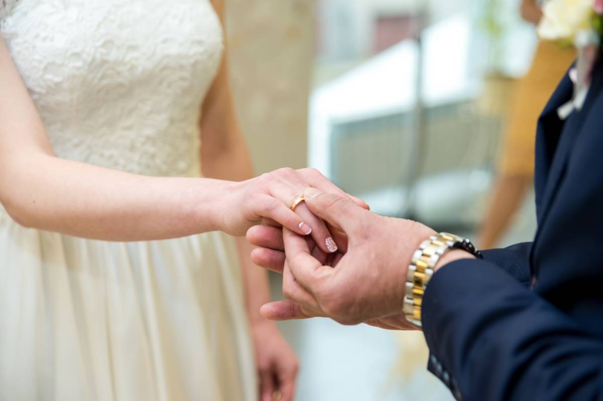 A groom slides a band onto the finger of his bride after deciding to buy wedding bands for himself and his bride-to-be.