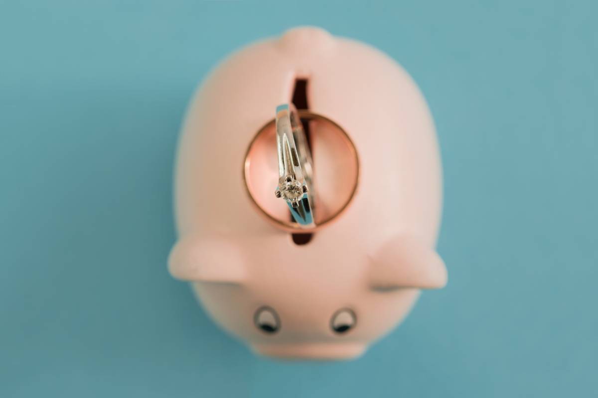 A ring sits perfectly balanced to fall into a miniature piggy bank which represents saving for an engagement ring fund.