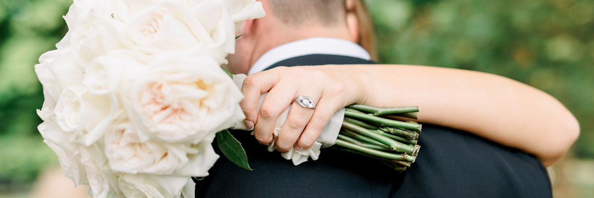 Bride embracing groom, her arms wrapped around his neck, showcasing engagement ring.